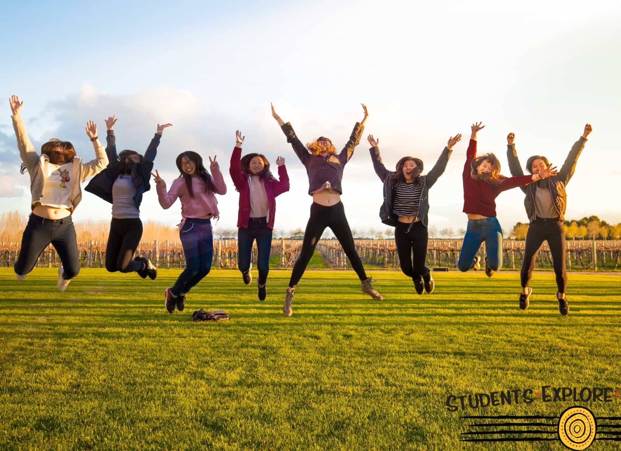 Students in a jump pose at a grass field