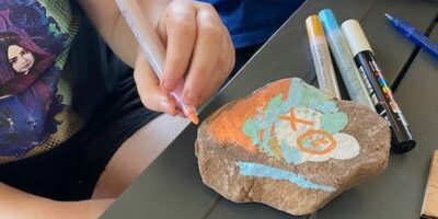 A camp participant creating an art piece on a rock during an arts & crafts activity on camp